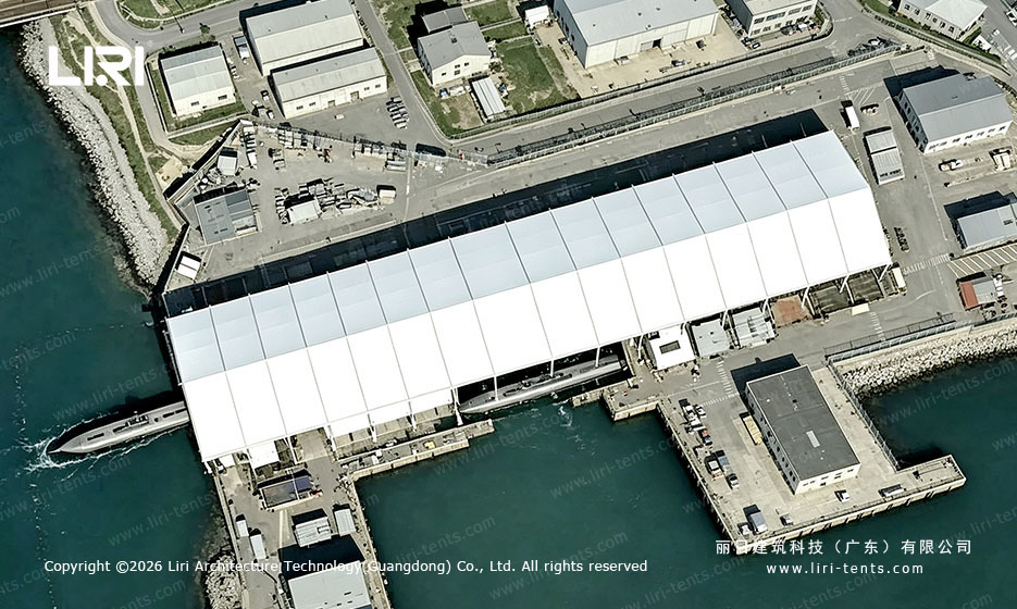 Aerial view of a white clear-span tent beside a shipyard dock