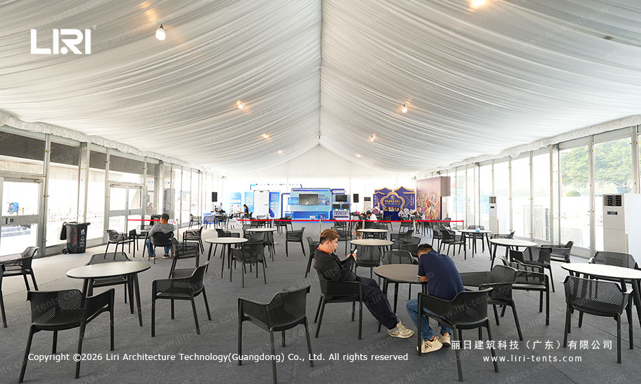 Dining tables and chairs inside a white event tent with a stage area at the far end