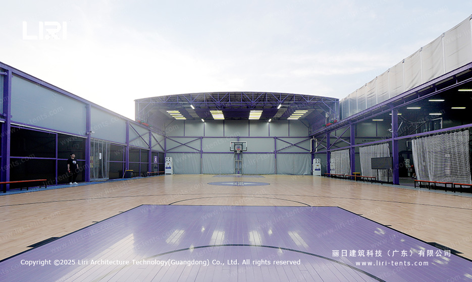 Wide interior showing multiple basketball hoops under arched purple truss roof with vinyl flooring