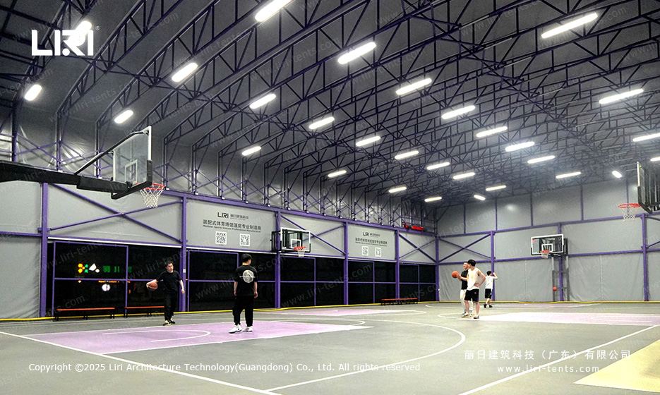 Players shooting hoops inside purple framed retractable roof basketball hall at dusk