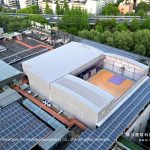 Aerial view of purple twin retractable basketball court tent on a city rooftop between solar panel arrays