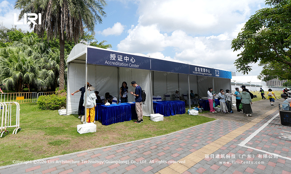 Small A-frame accreditation tent at a race track with staff handling passes at blue-clothed tables along the side