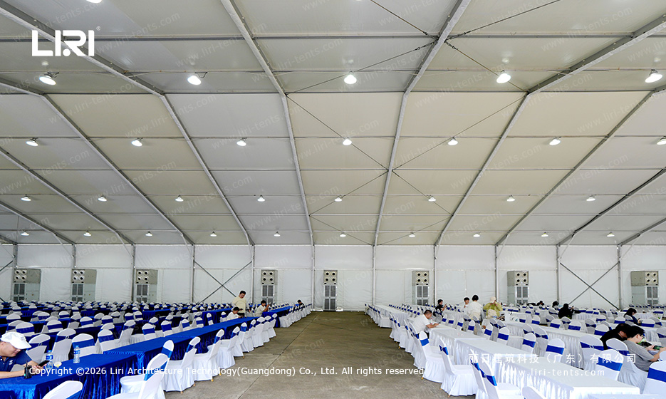 Full interior view of a clear span spectator lounge tent with rows of long blue-clothed tables and roof-mounted air conditioning at a race track