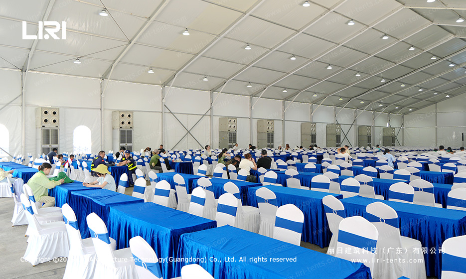Wide interior view of a clear span event tent set up with rows of blue-clothed tables and white chairs for race track spectators and VIP guests