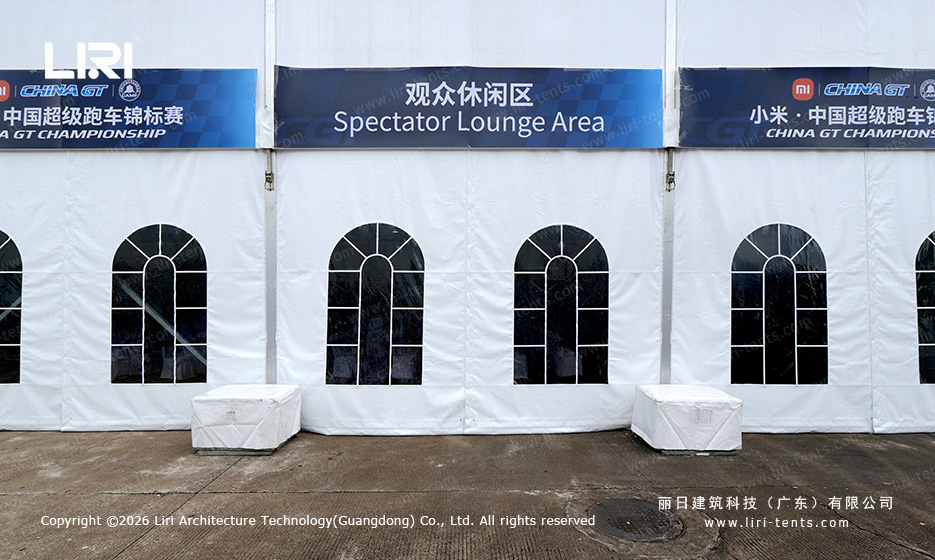 Arched glass windows along a long white clear span event tent wall at a race track, set up for spectators during a motorsport weekend