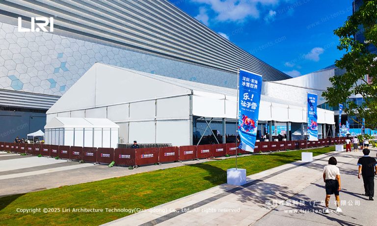 Aerial exterior view of a large A-frame clear span event tent set up next to a modern commercial building for an opening ceremony