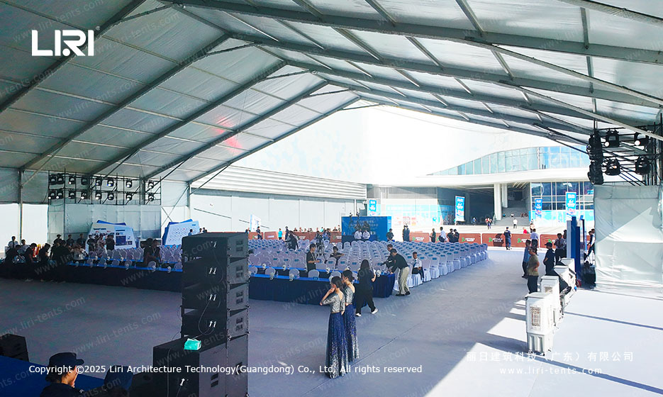 Interior of a large clear span event tent with stage, truss rigging, and rows of chairs for a Shenzhen opening ceremony