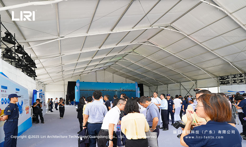 Crowd and security personnel near the stage backdrop inside a clear span event tent at a Shenzhen opening ceremony