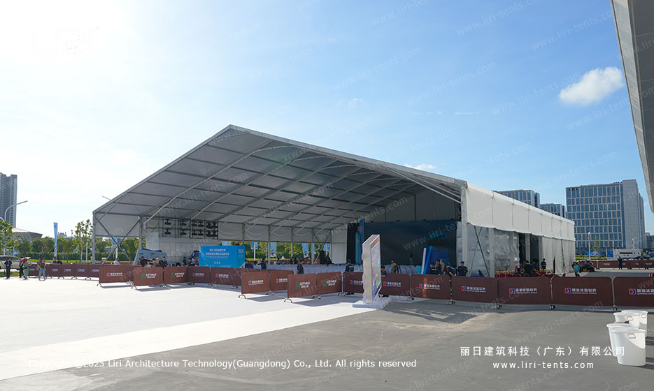 Wide exterior view of a large white A-frame event tent with sound and lighting truss visible through the open side